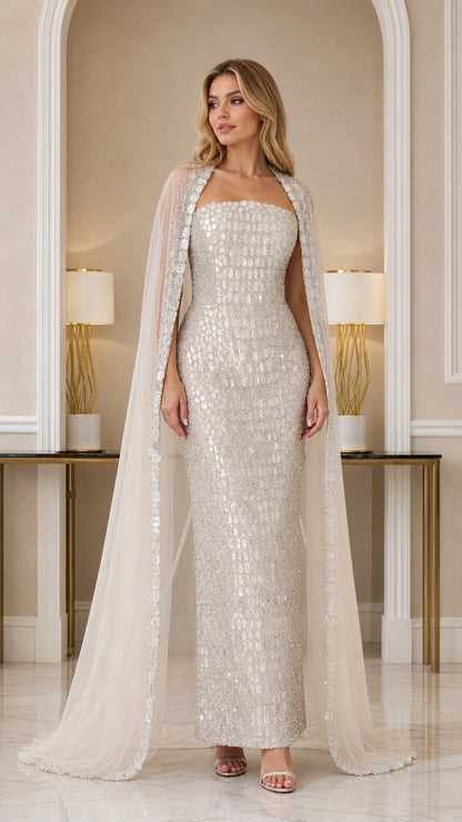 Front view of model wearing Champagne strapless embellished column gown with sheer cape