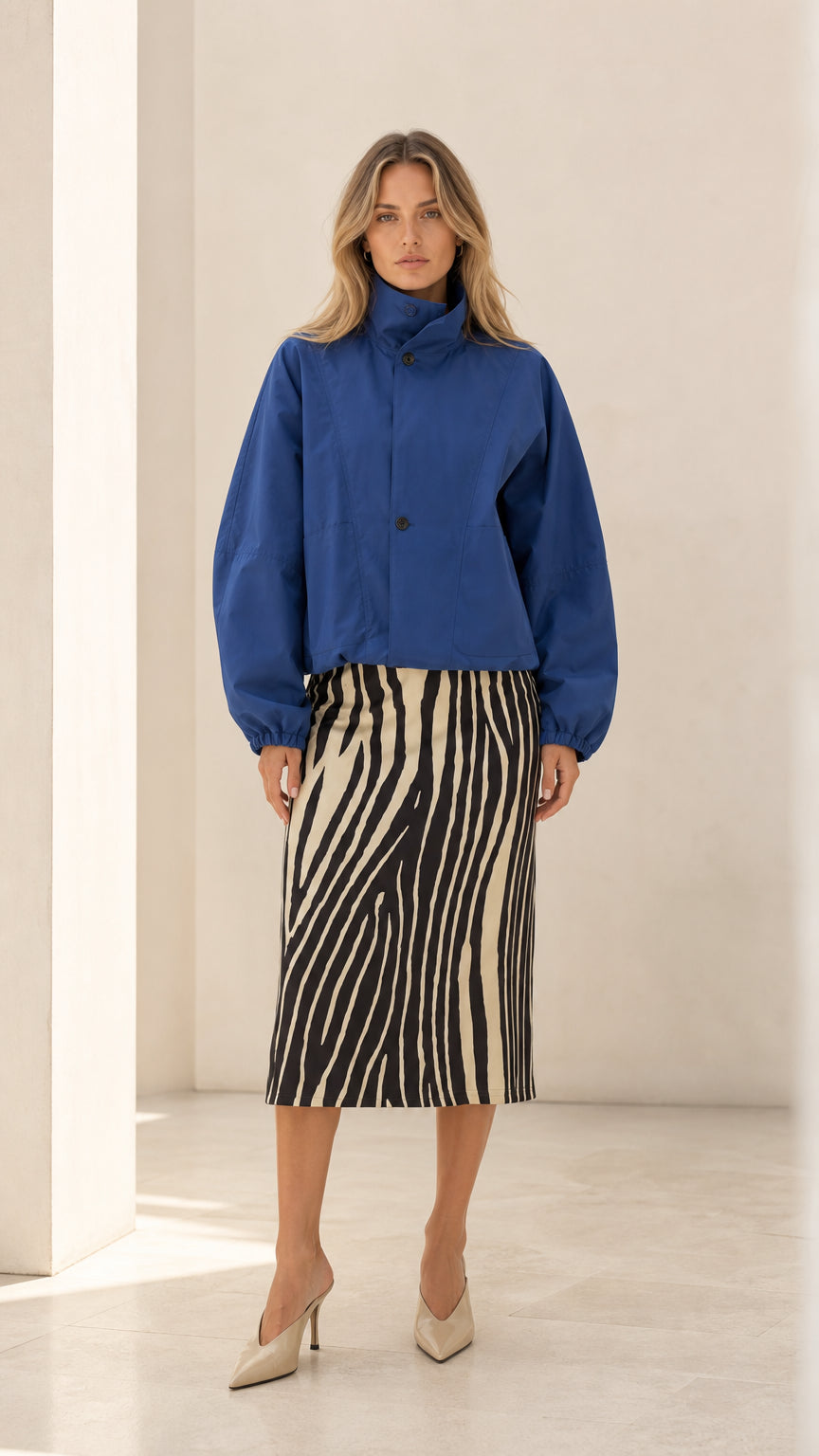 Front full view of woman wearing royal blue high neck cropped blouson jacket with zebra midi skirt