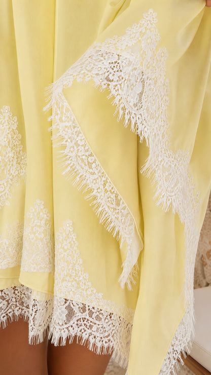 Close-up detail of white floral eyelash lace trim on pastel yellow fabric
