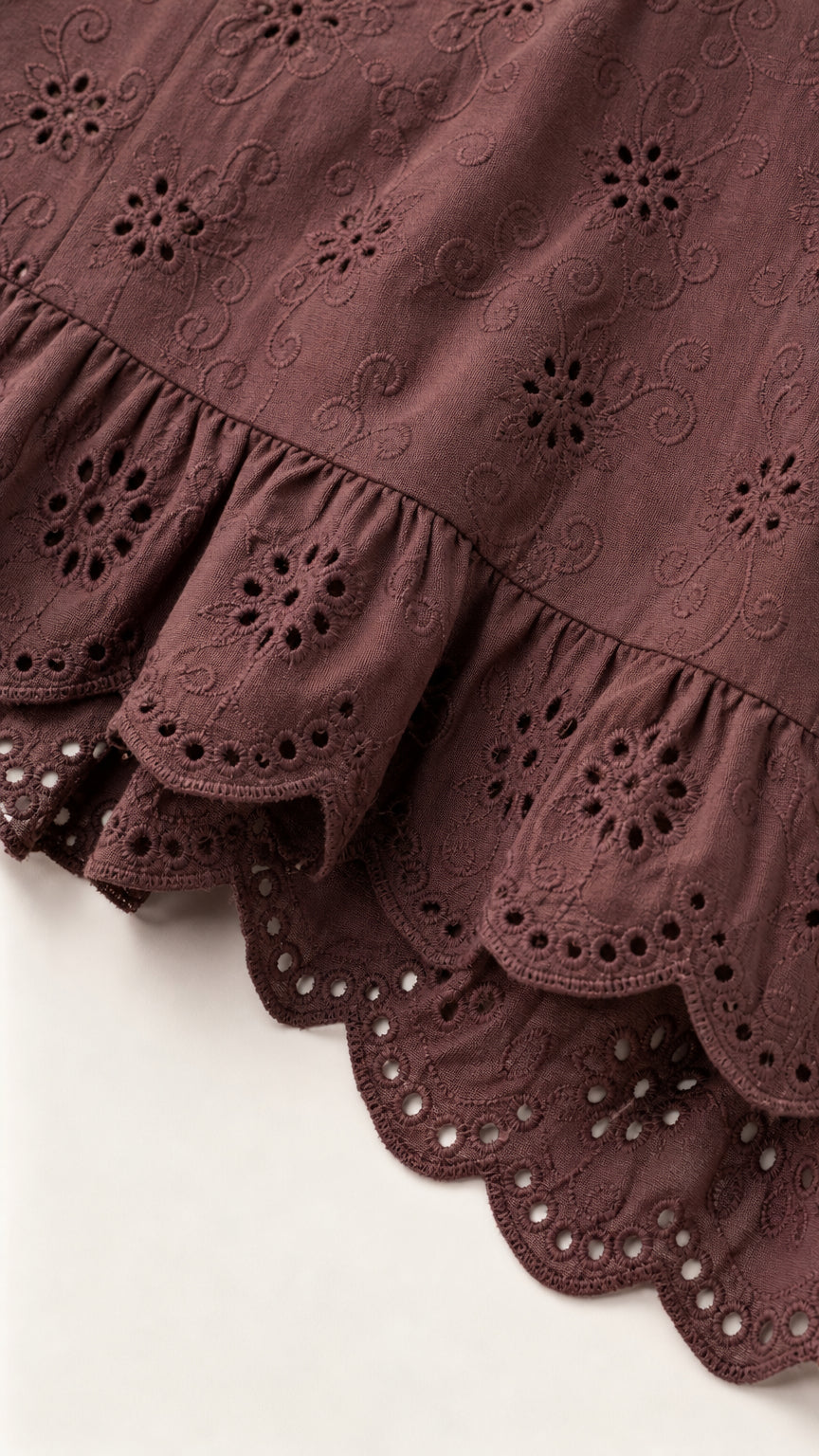 Close-up detail of plum brown eyelet embroidery and scalloped ruffled hem