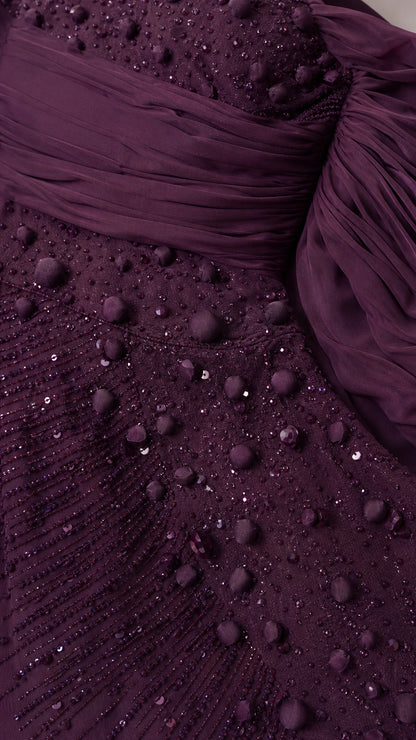 Close-up of intricate dark plum beading, sequins, and ruched draped sleeve detail