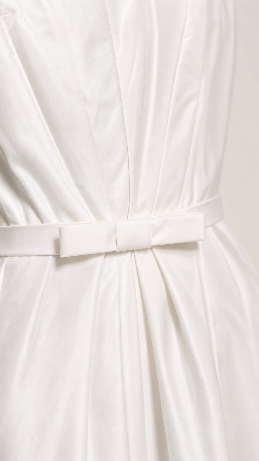 Close-up detail of pleated bodice fabric and waist bow on white midi dress