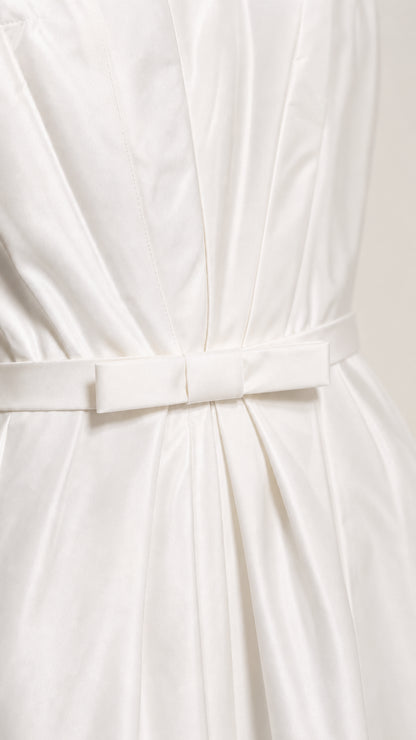 Close-up detail of pleated bodice fabric and waist bow on white midi dress