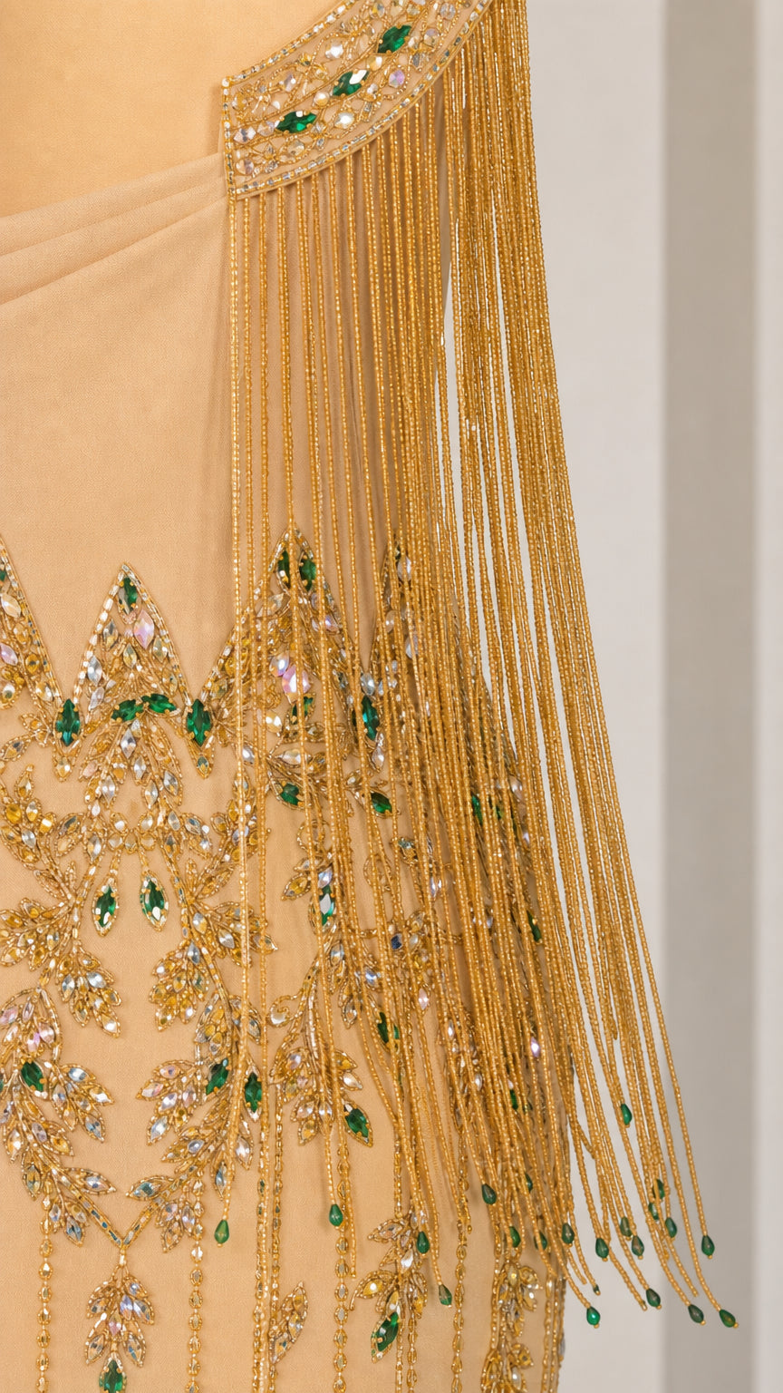 Close-up detail of gold fringe beadwork and green crystal embroidery on evening gown