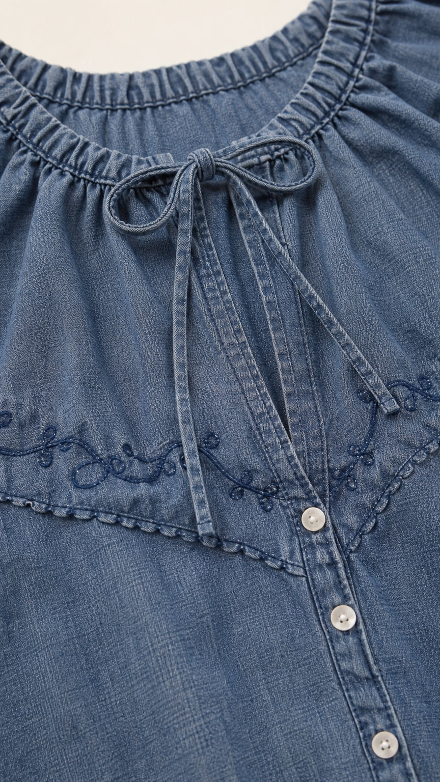 Close-up detail of Denim Blue gathered tie neckline, tonal floral embroidery, and buttons